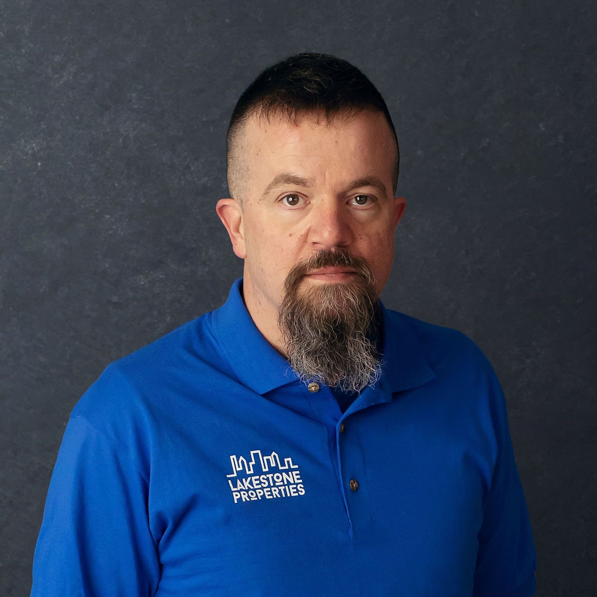 a man with a beard wears a blue shirt that says lakestone properties