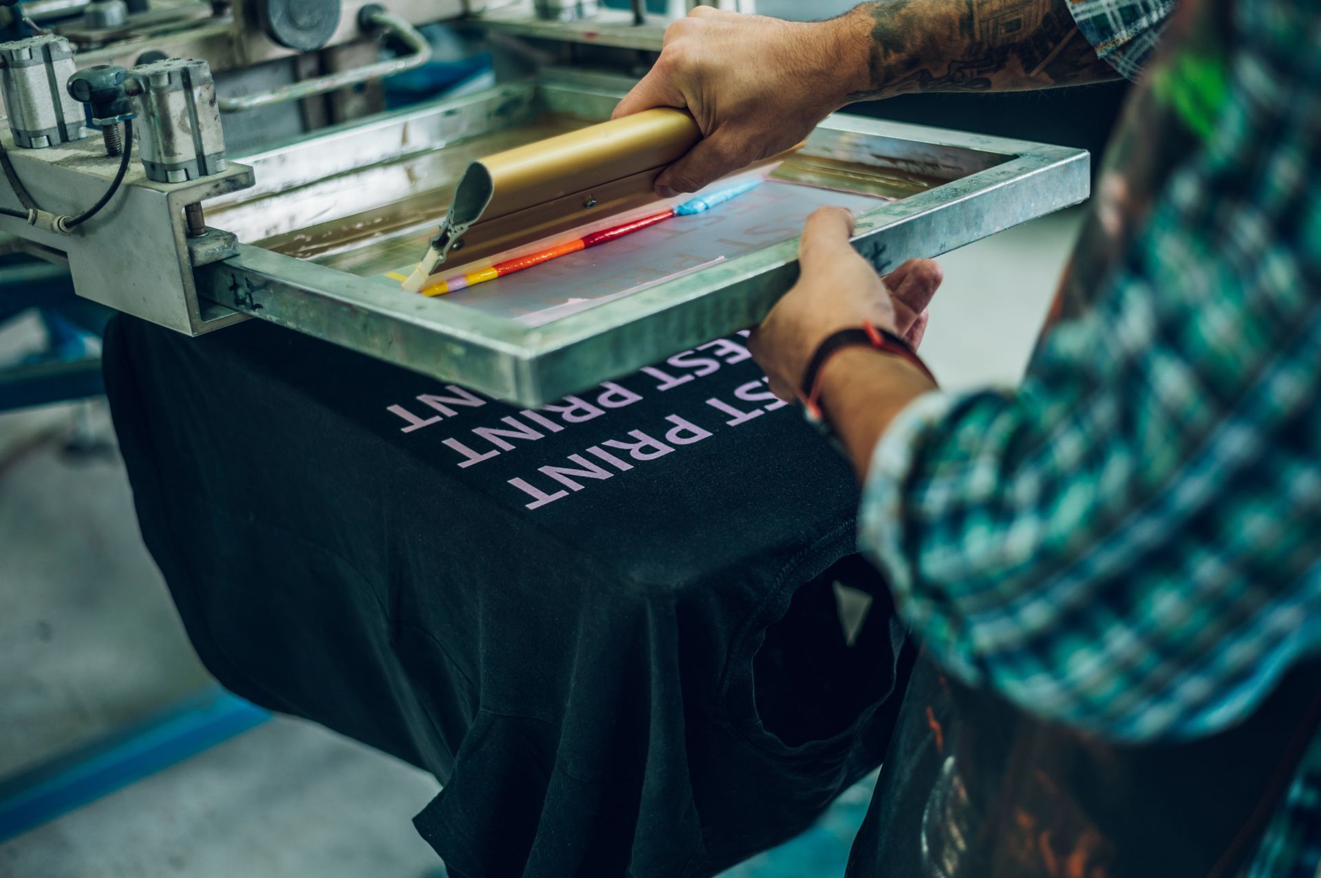 Close-up of a worker pressing ink on a frame while using the printing machine for custom workwear.