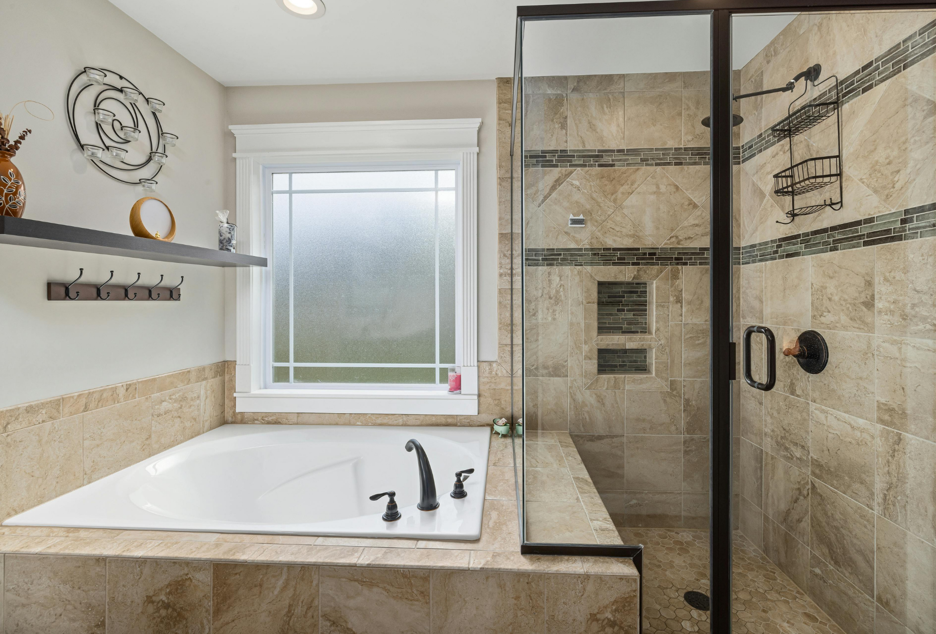 Bathroom with a soaking tub, glass shower, and frosted window. Beige tiles cover the walls and floor, with black fixtures.