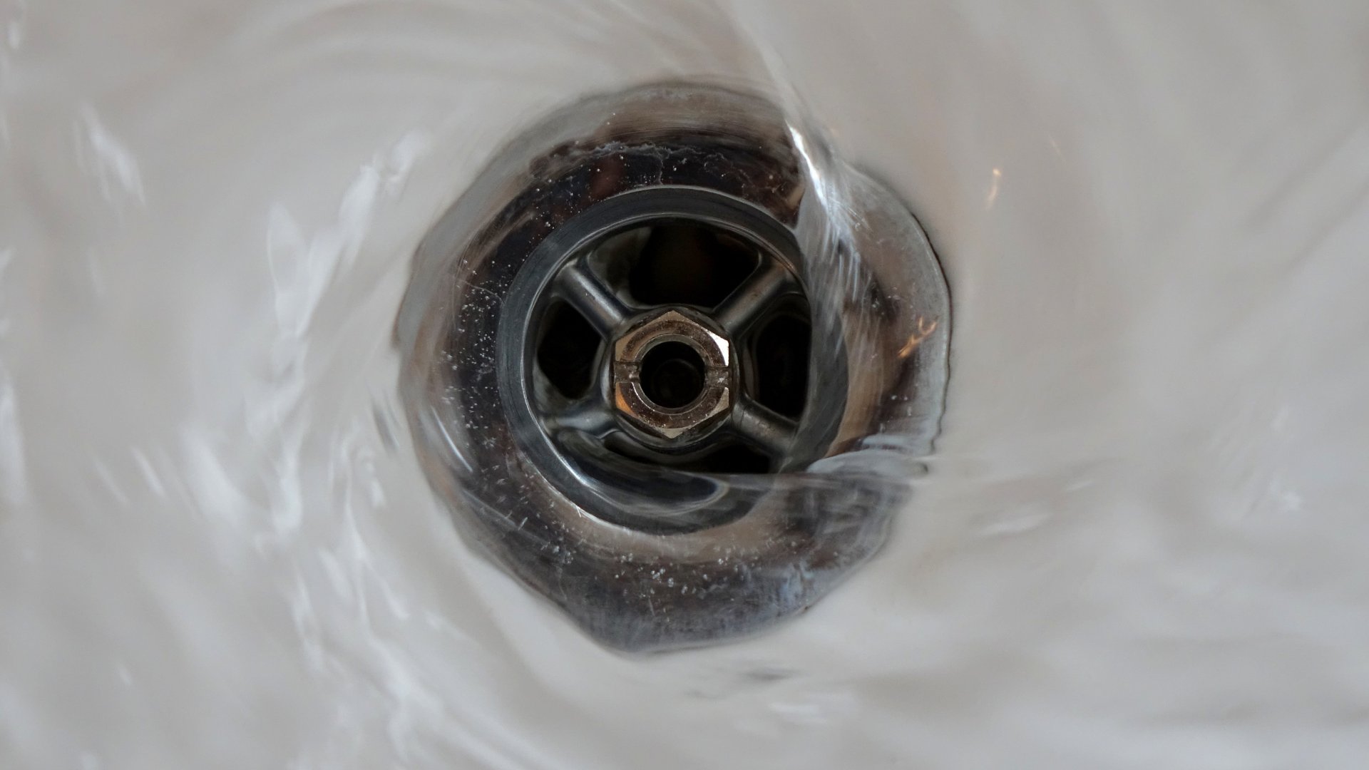 Water swirling towards a chrome drain in a white sink.