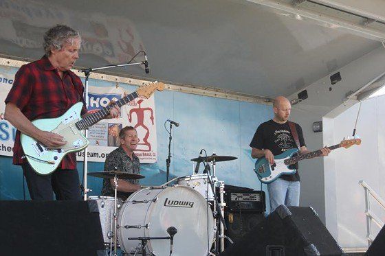 Three men are playing guitars and drums on a stage.