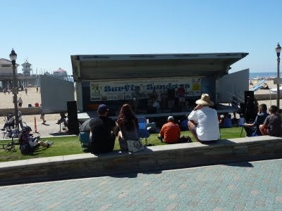 A group of people sitting on a wall watching a band on stage