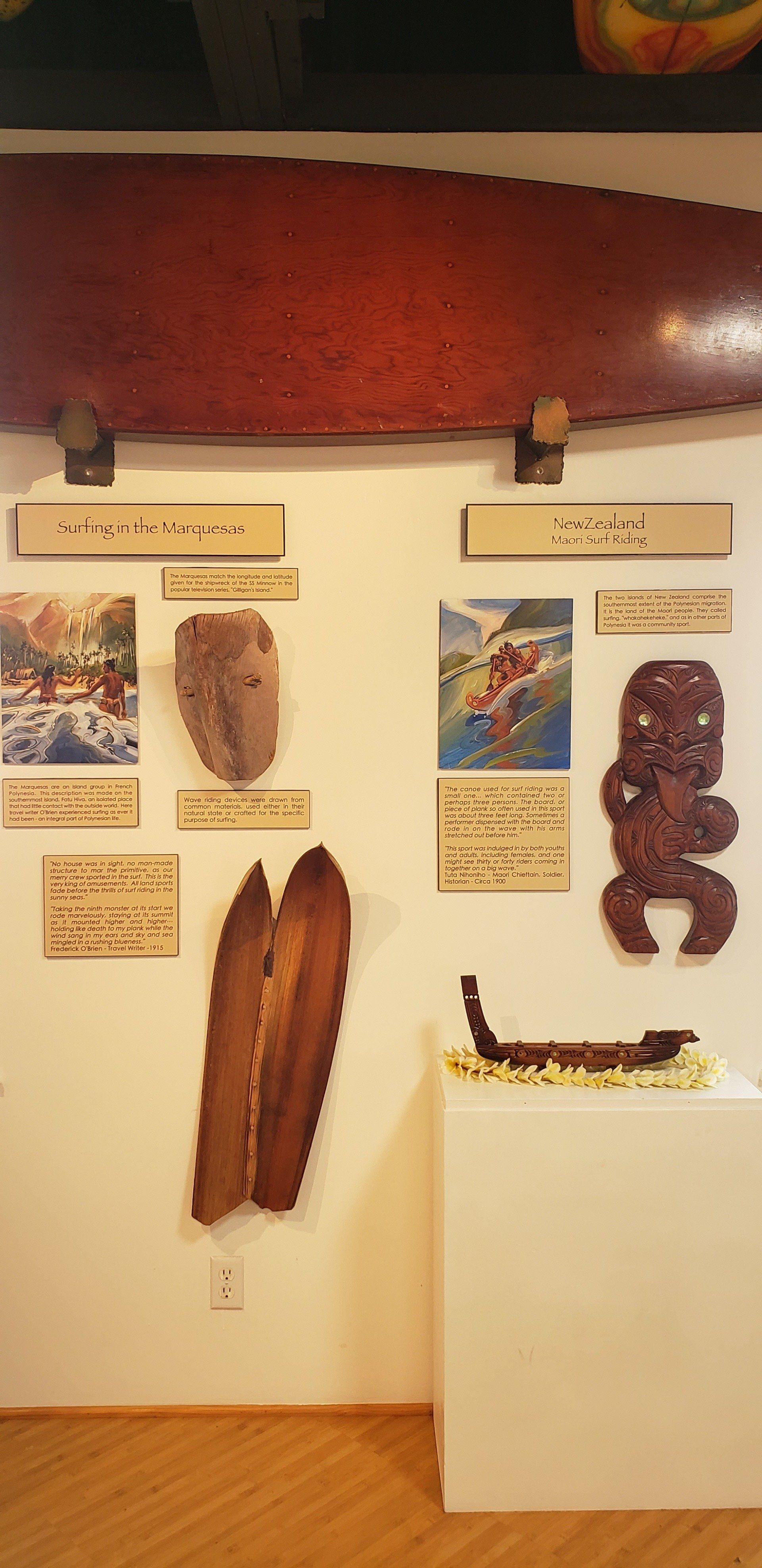 A wooden surfboard is hanging on a wall next to a painting.