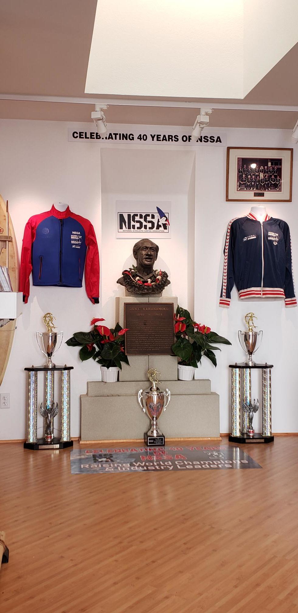 A room with a statue , trophies , and jackets on the wall.