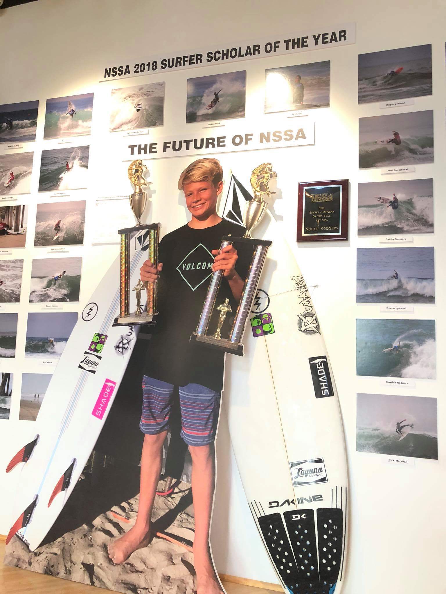 A young man holding a trophy next to a surfboard