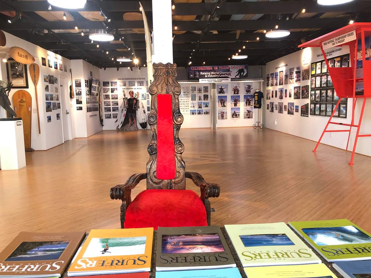 A red chair is sitting in a room surrounded by books