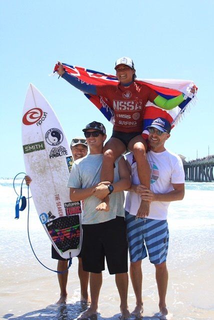 A man carrying a girl on his shoulders while holding a surfboard that says nessi on it
