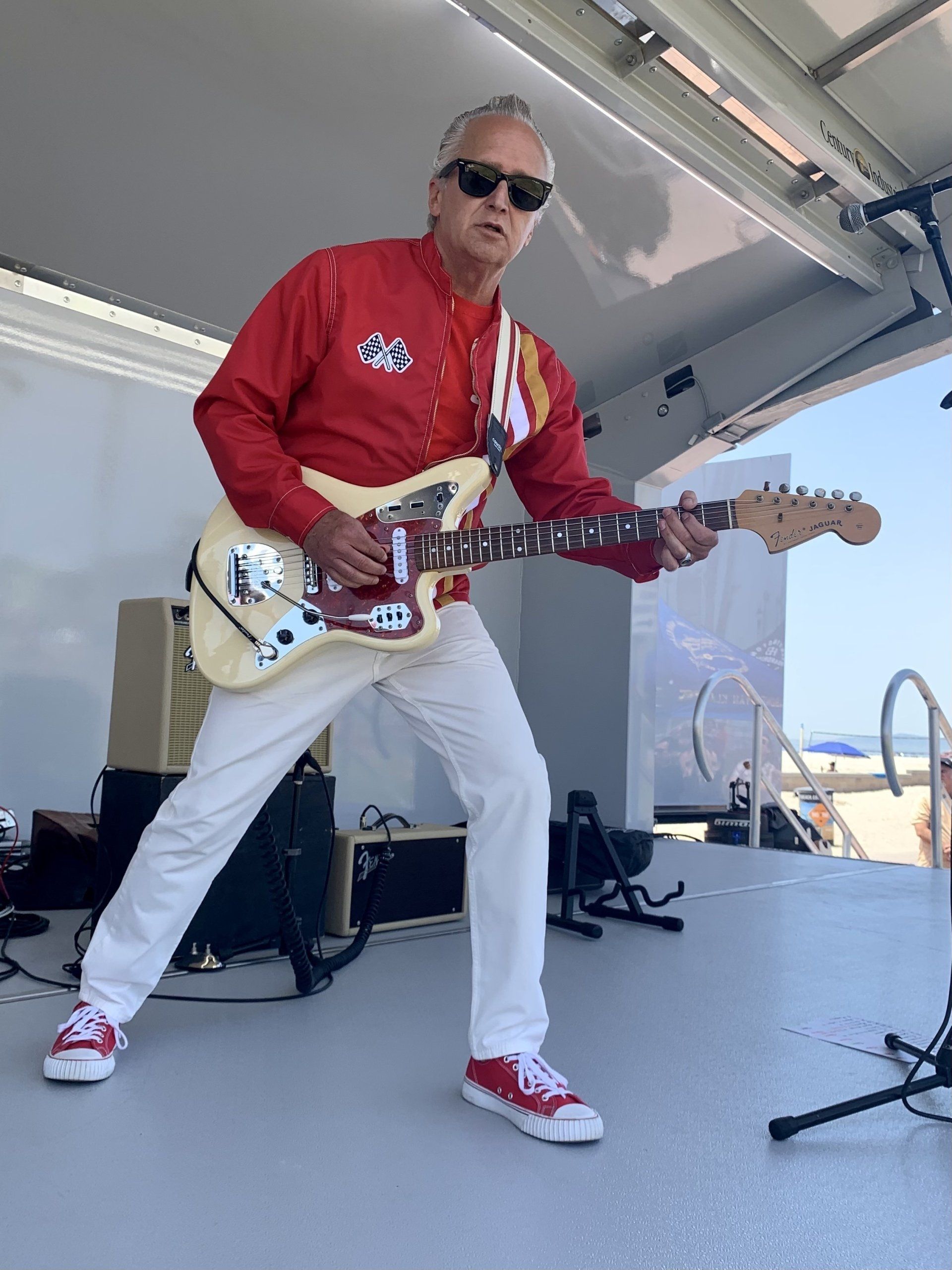 A man in a red shirt and white pants is playing a guitar on a stage.