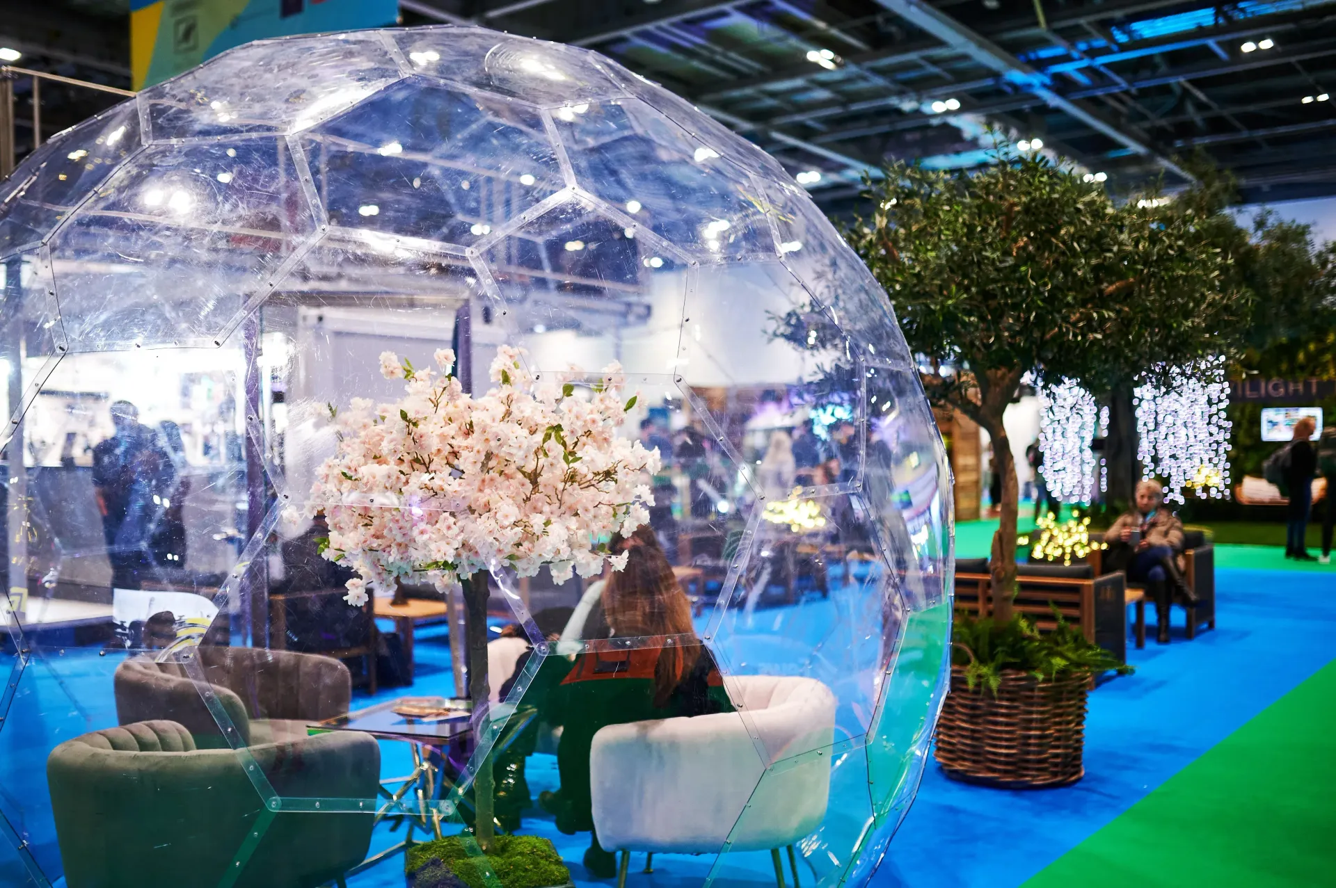 A woman is sitting inside of a clear dome at a convention.