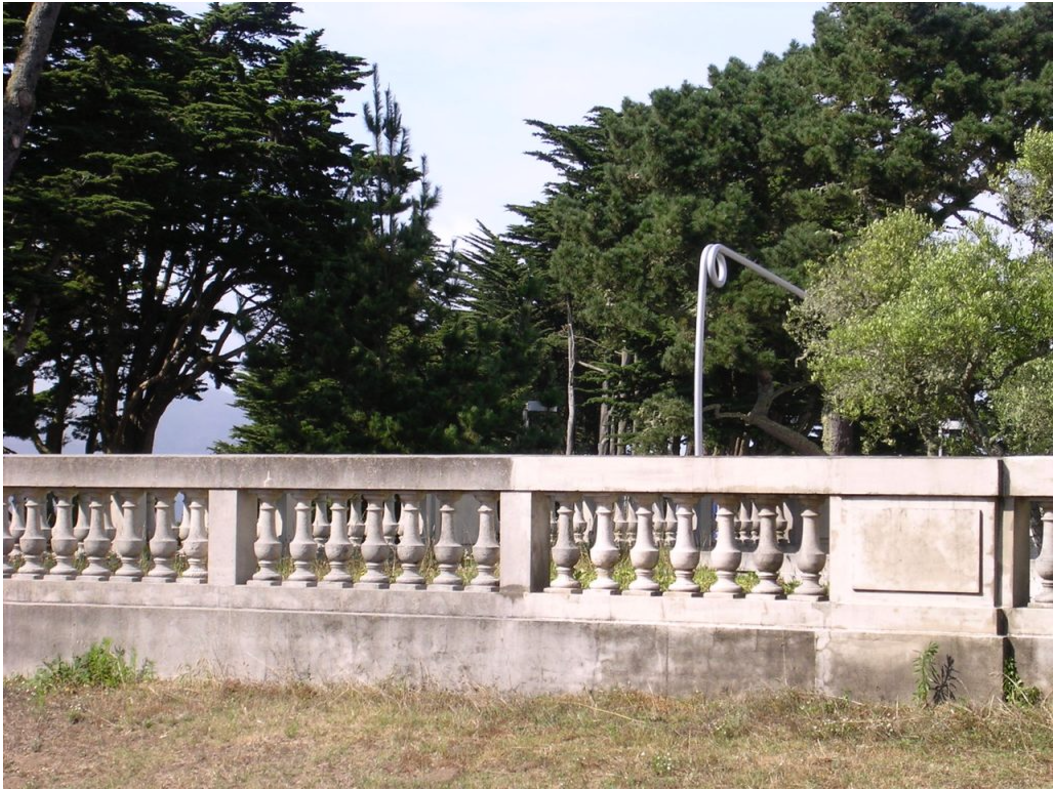 A concrete wall with a railing and trees in the background