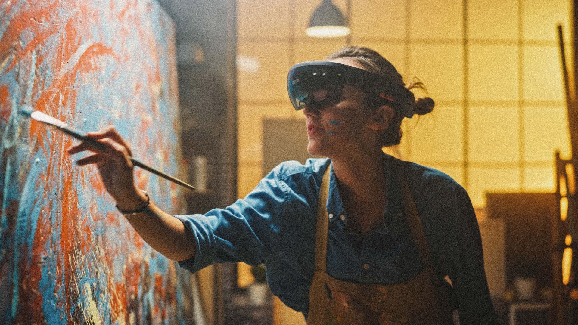 Artist painting on a large canvas, wearing a visor and work clothes in a studio with warm light.