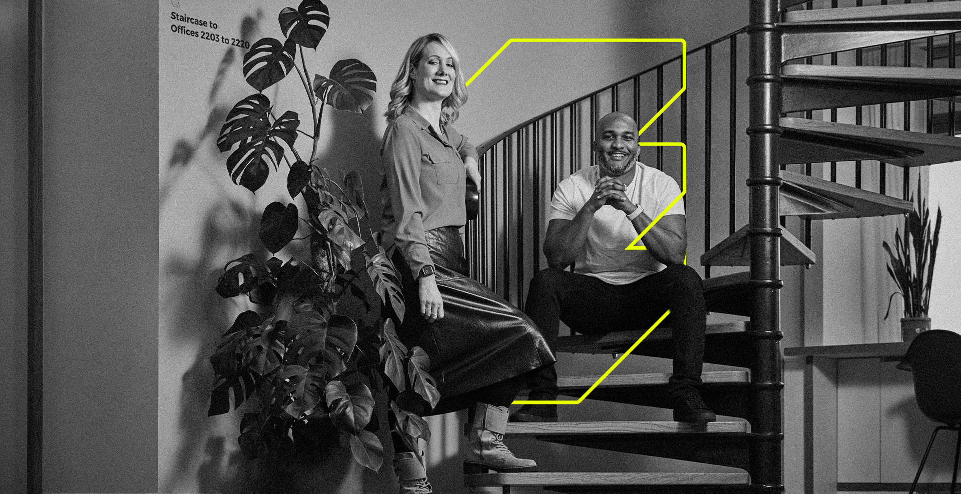 Woman and man posing on staircase, near a plant. Man seated with hand to his chin; woman standing. Monochrome.