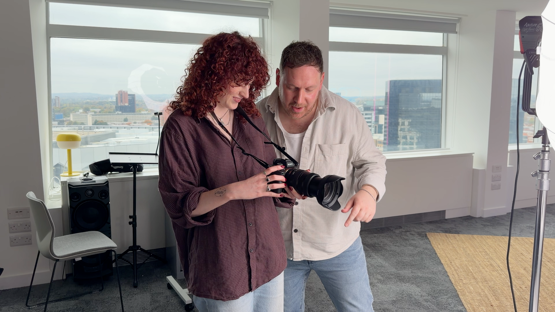 Two people looking at a camera in a studio with city views.