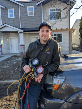 Man in a hoodie holding gauges, leaning on a vehicle in front of a house.