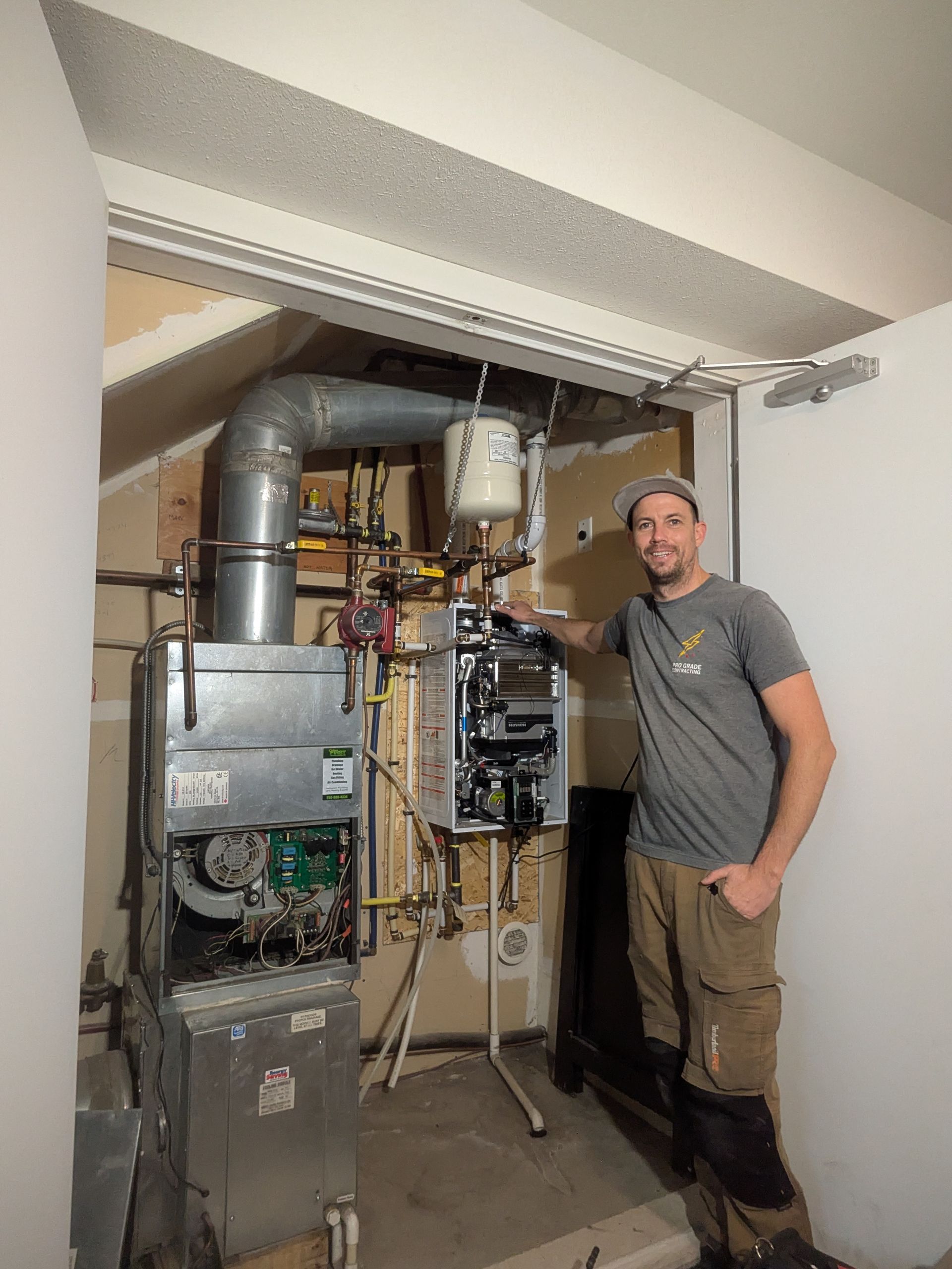 Man standing next to a furnace and boiler in a utility room. He is smiling and gesturing towards the equipment.