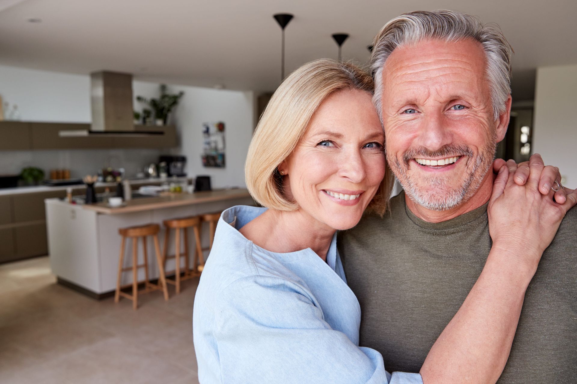 Couple at a kitchen counter, man holding coffee, woman reading a book.
