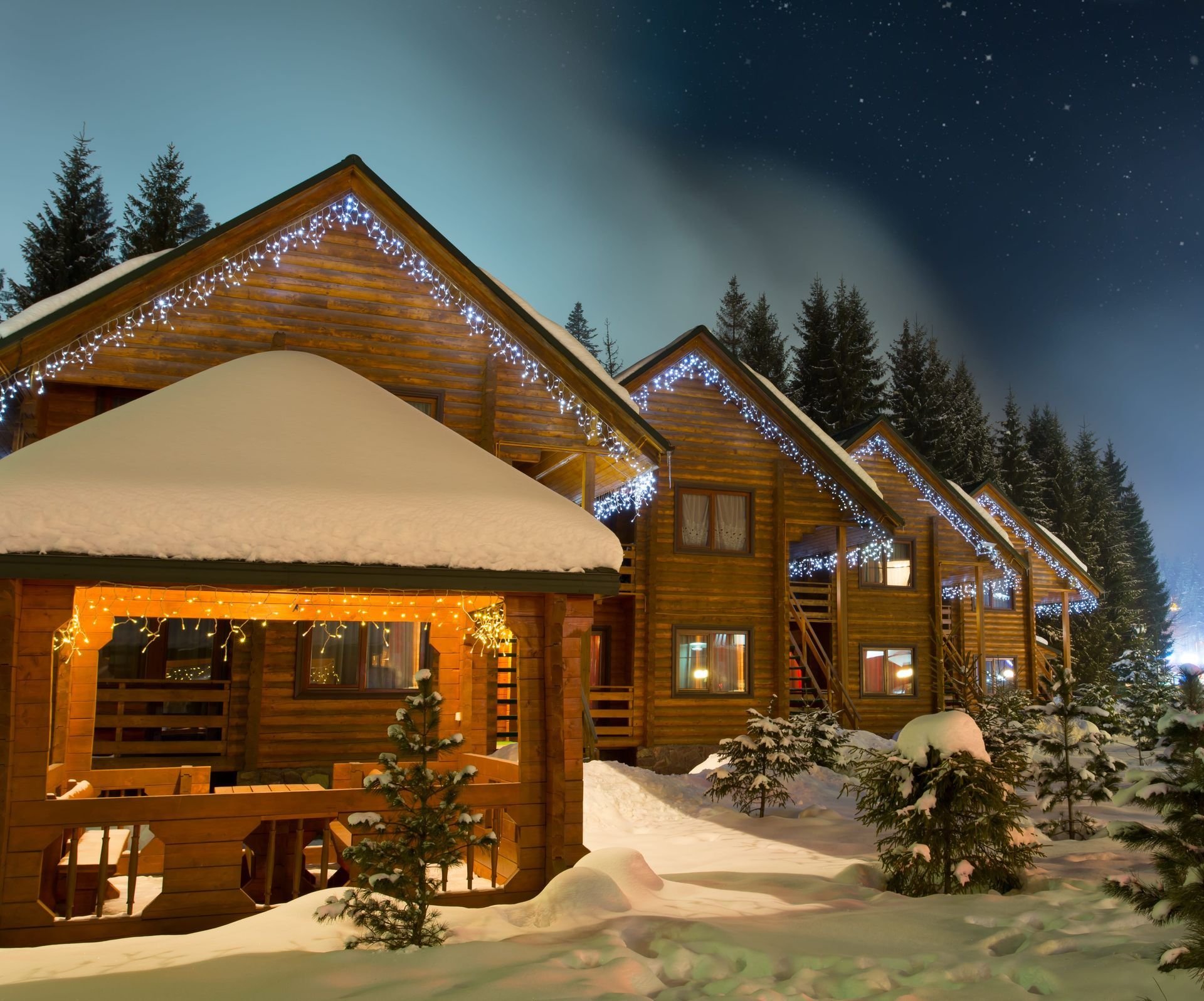 Snow-covered wooden cabins with twinkling lights under a starry night sky.
