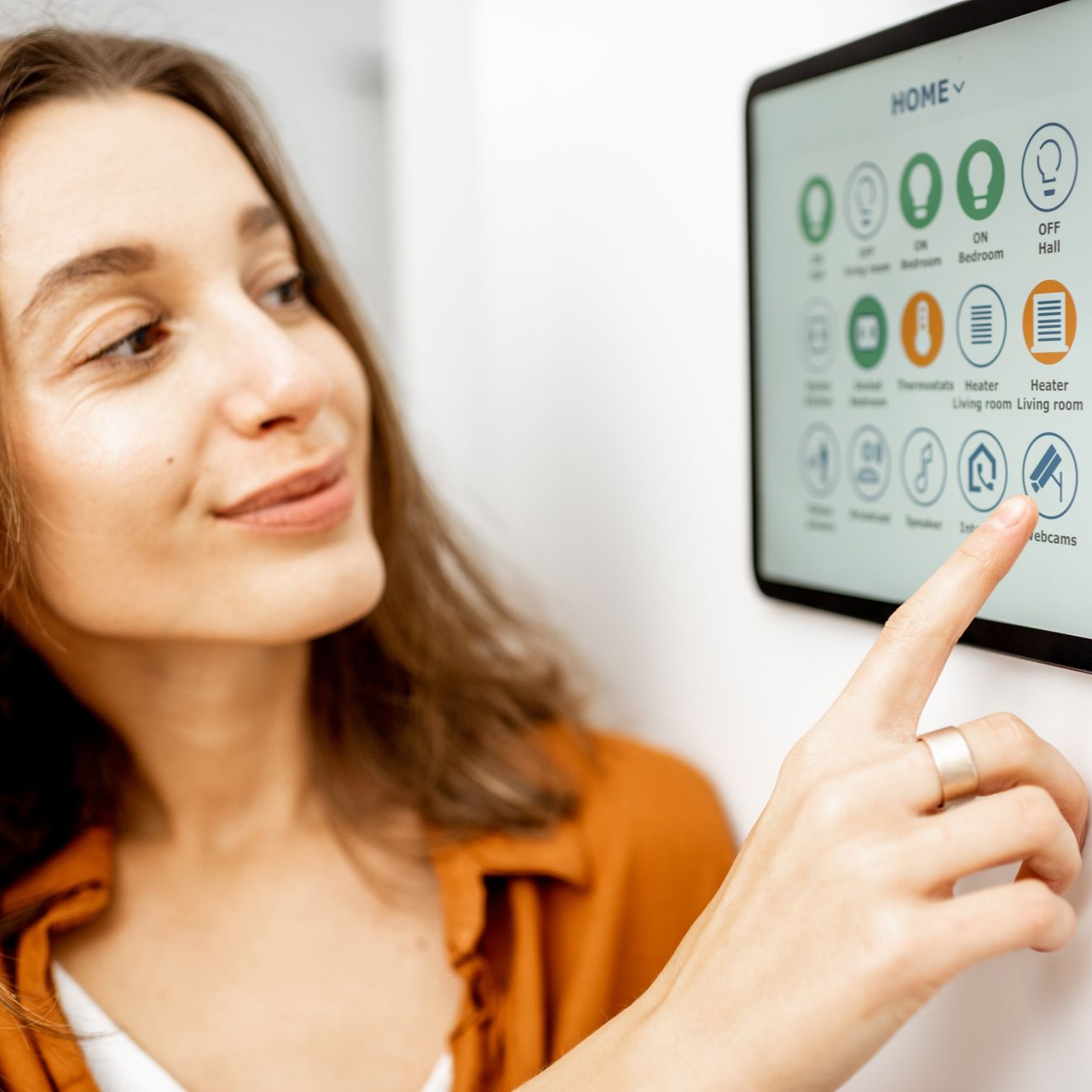 Woman interacting with a smart home control panel on a white wall; touching an icon.