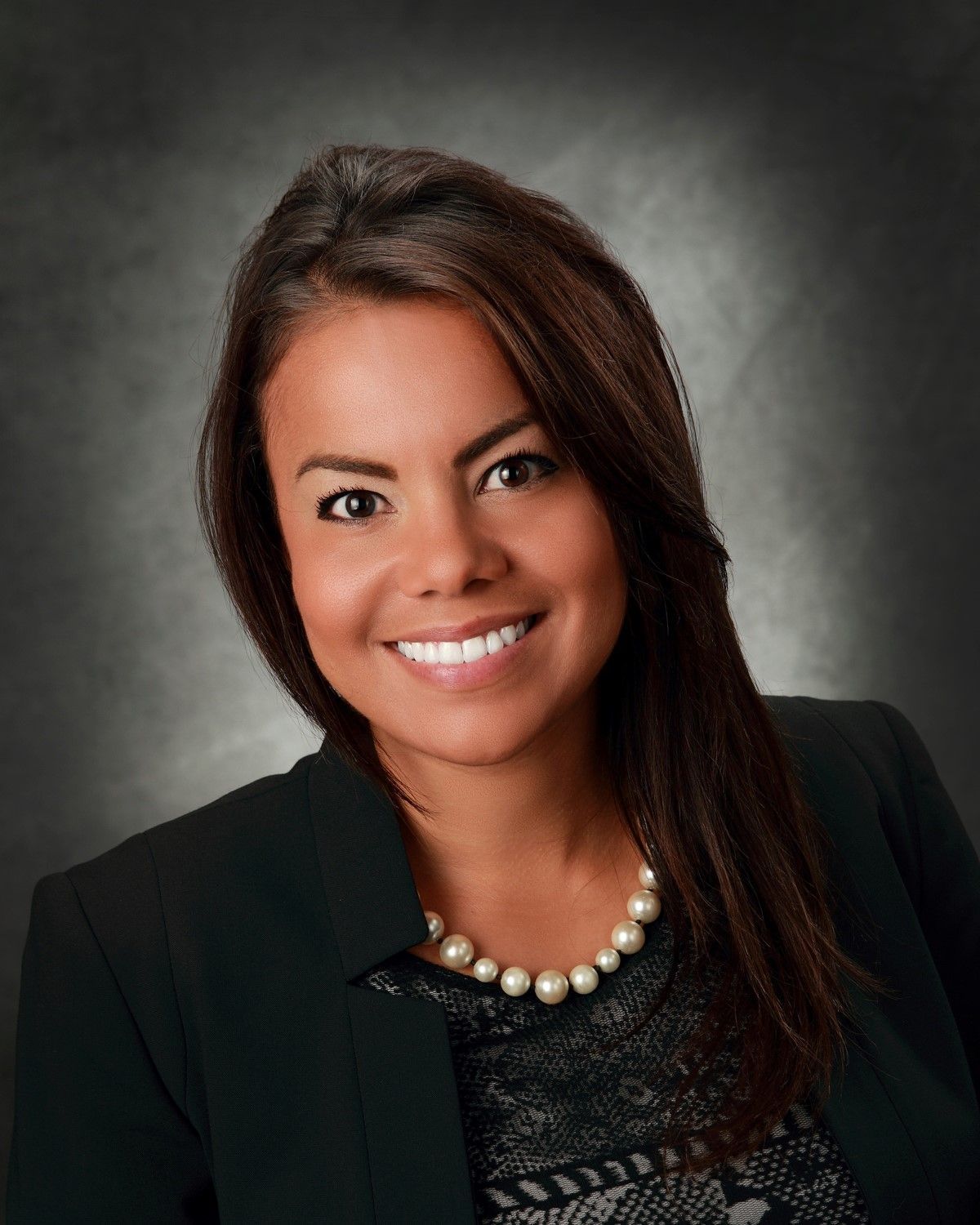 A woman wearing a black jacket and pearls smiles for the camera