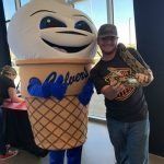 A man is standing next to an ice cream cone mascot.