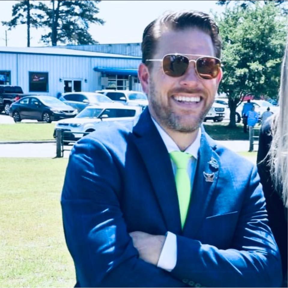 A man in a suit and tie is smiling with his arms crossed
