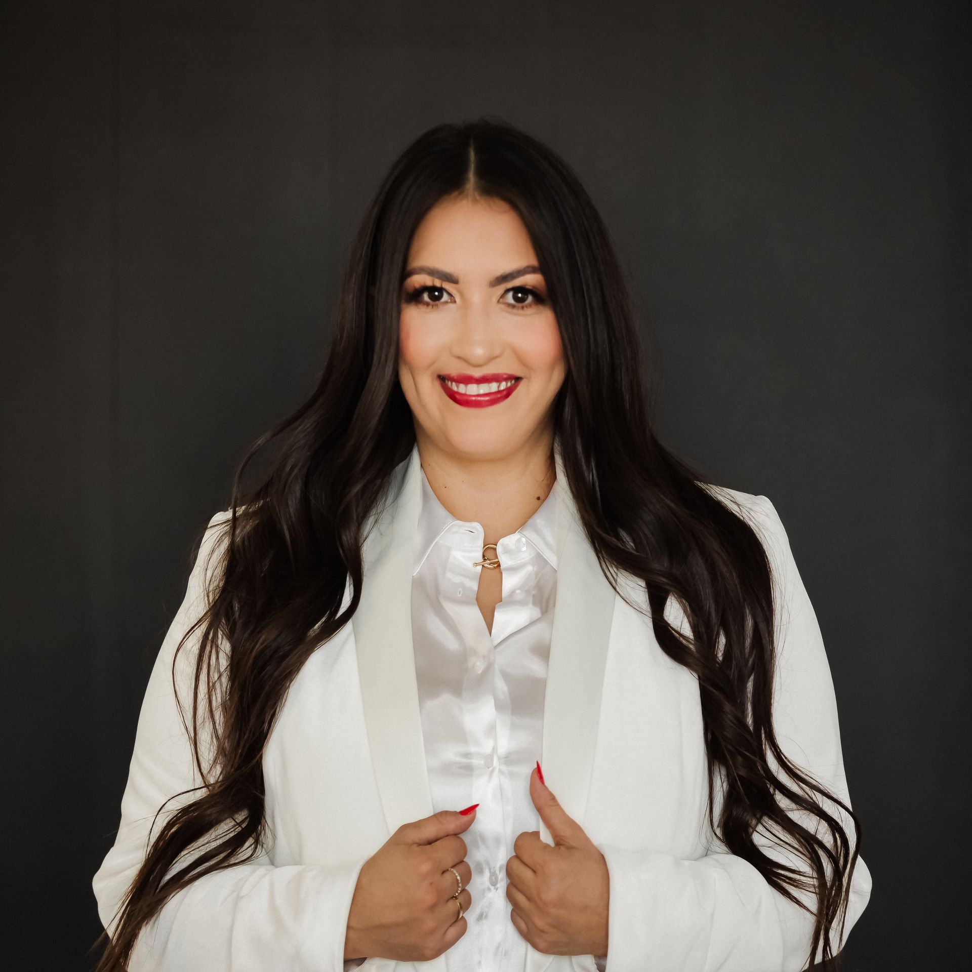 A woman with long hair is wearing a white jacket and smiling.