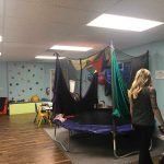 A woman is standing in a room with a trampoline and a climbing wall.