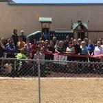A large group of people are standing behind a chain link fence.