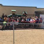 A large group of people are standing in front of a chain link fence.