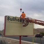 A man is sitting on top of a large billboard.