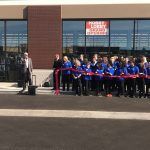 A group of people are standing in front of a building cutting a red ribbon.
