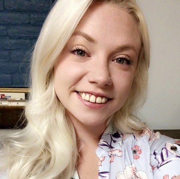 A woman with blonde hair is smiling and wearing a floral shirt