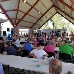A large group of people are sitting at tables under a canopy.