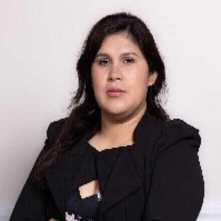 A woman in a black jacket is sitting in front of a white wall.