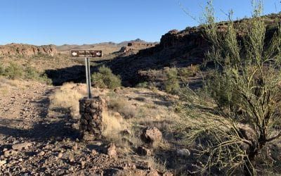 A sign in the middle of a desert with mountains in the background.