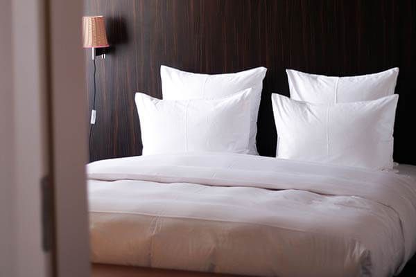A bed with white sheets and pillows in a hotel room
