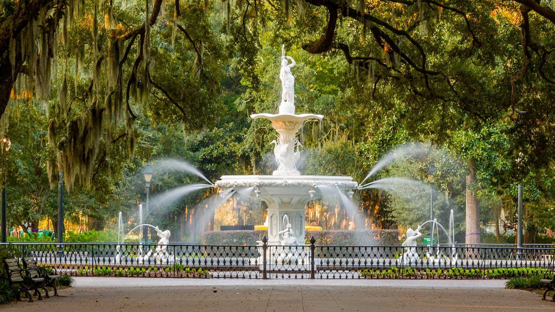 A fountain in a park surrounded by trees and benches.