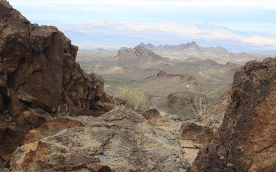 A view of a desert landscape from a rocky cliff with mountains in the background.