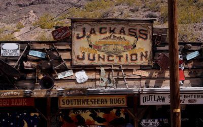 A sign for jackass junction is hanging on a wooden wall.
