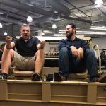 Two men are sitting on the back of a military vehicle.