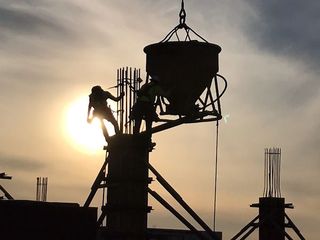 A silhouette of a construction site with the sun shining through the clouds