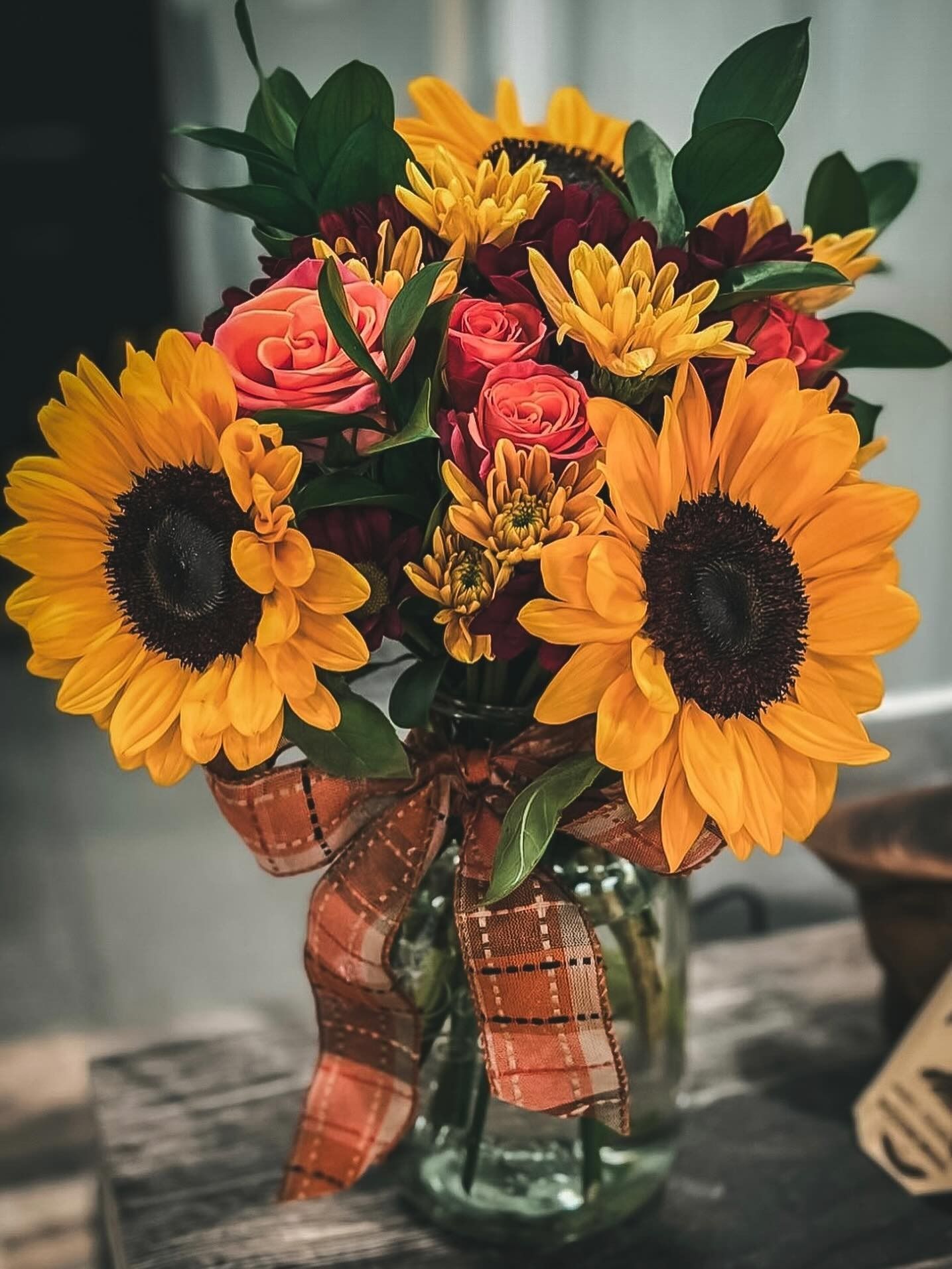 Bouquet of sunflowers and pink roses in a glass vase with a plaid ribbon