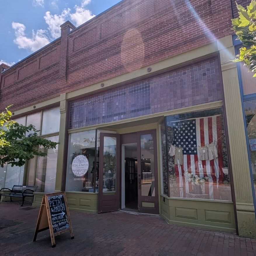 Storefront with large American flag display, brick facade, and sidewalk chalkboard sign on a sunny street