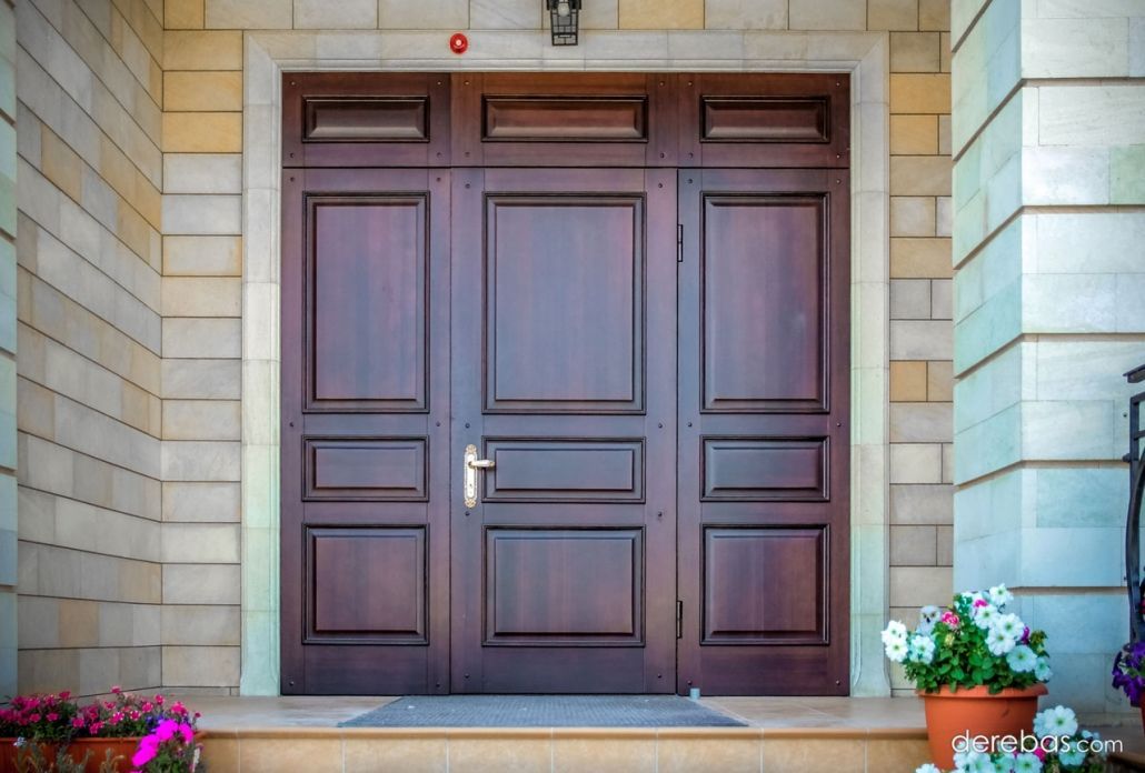 A large wooden door is sitting on a porch next to a pot of flowers.