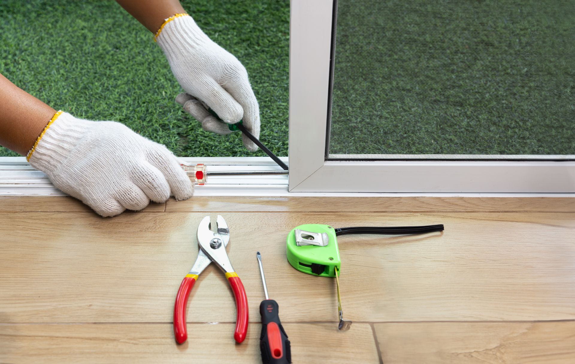 A person is fixing a sliding glass door with a screwdriver.