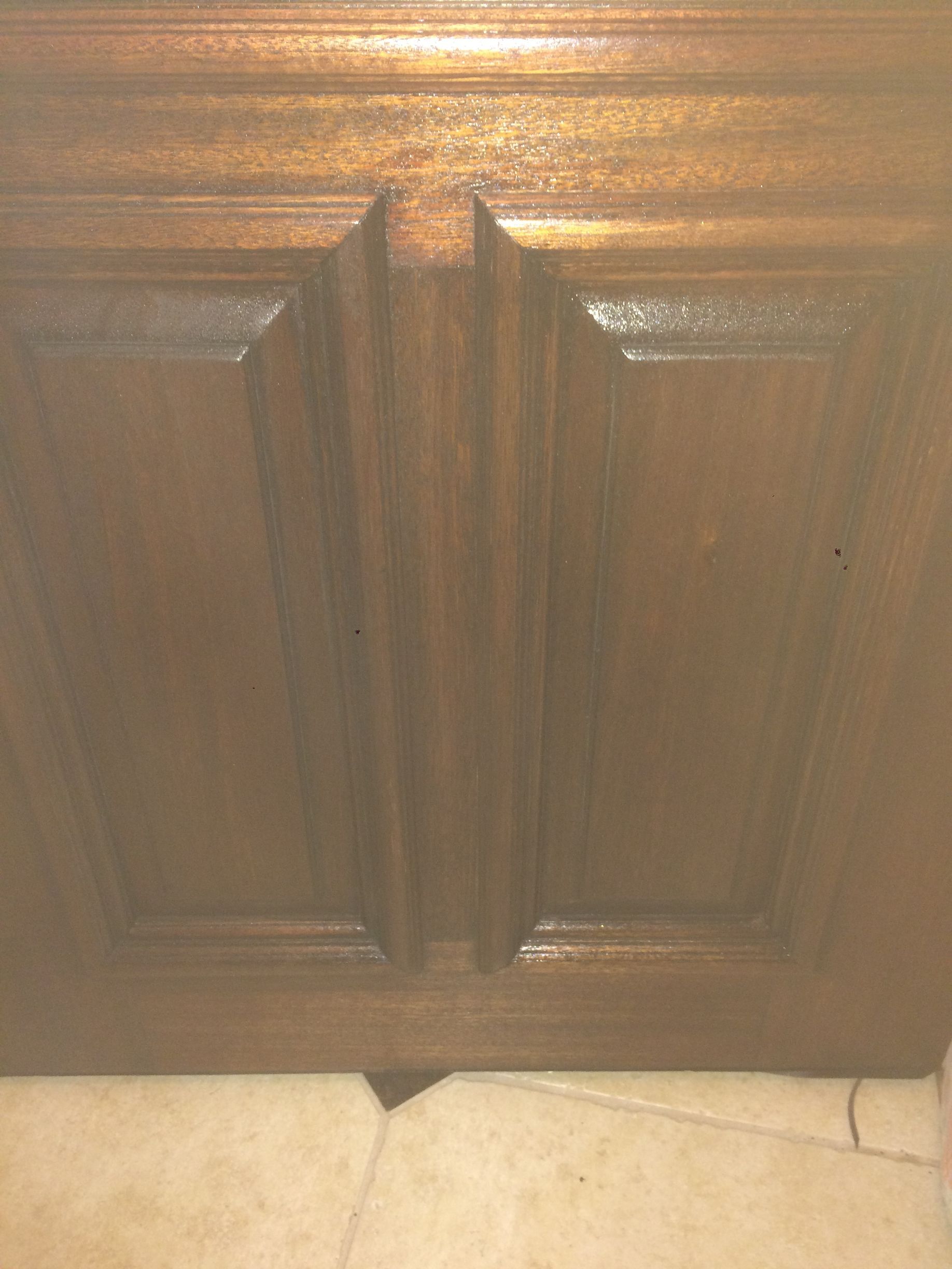 A close up of a wooden cabinet door on a tiled floor.