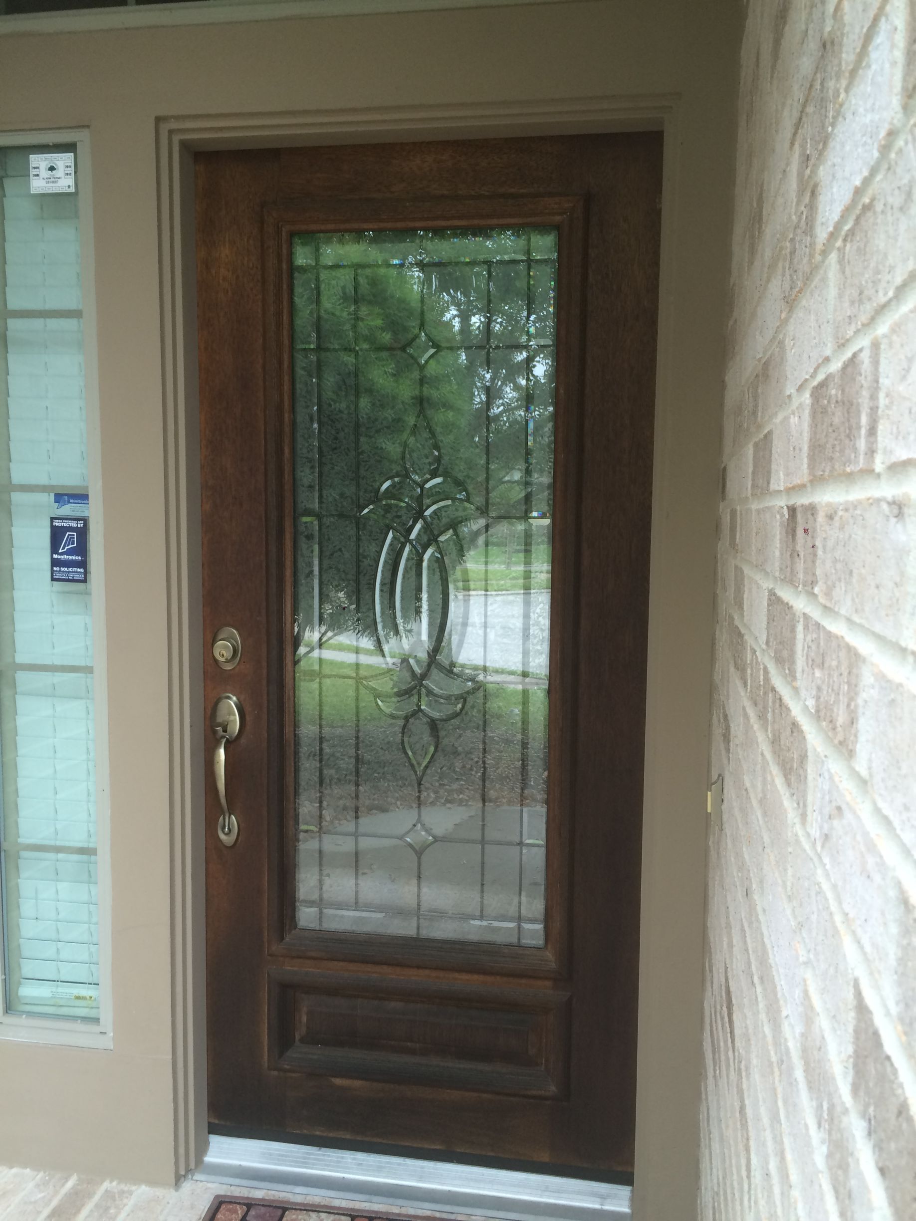 A wooden door with a stained glass window is on a brick wall.