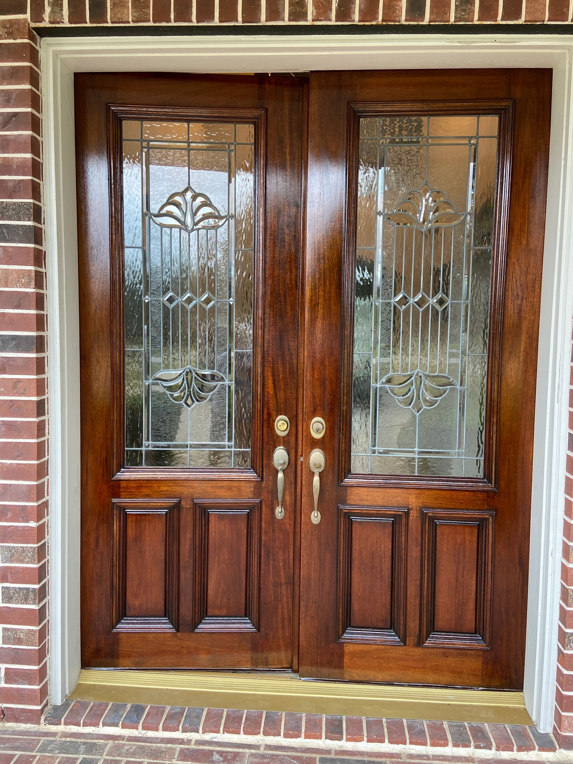 A pair of wooden doors with stained glass on a brick building.