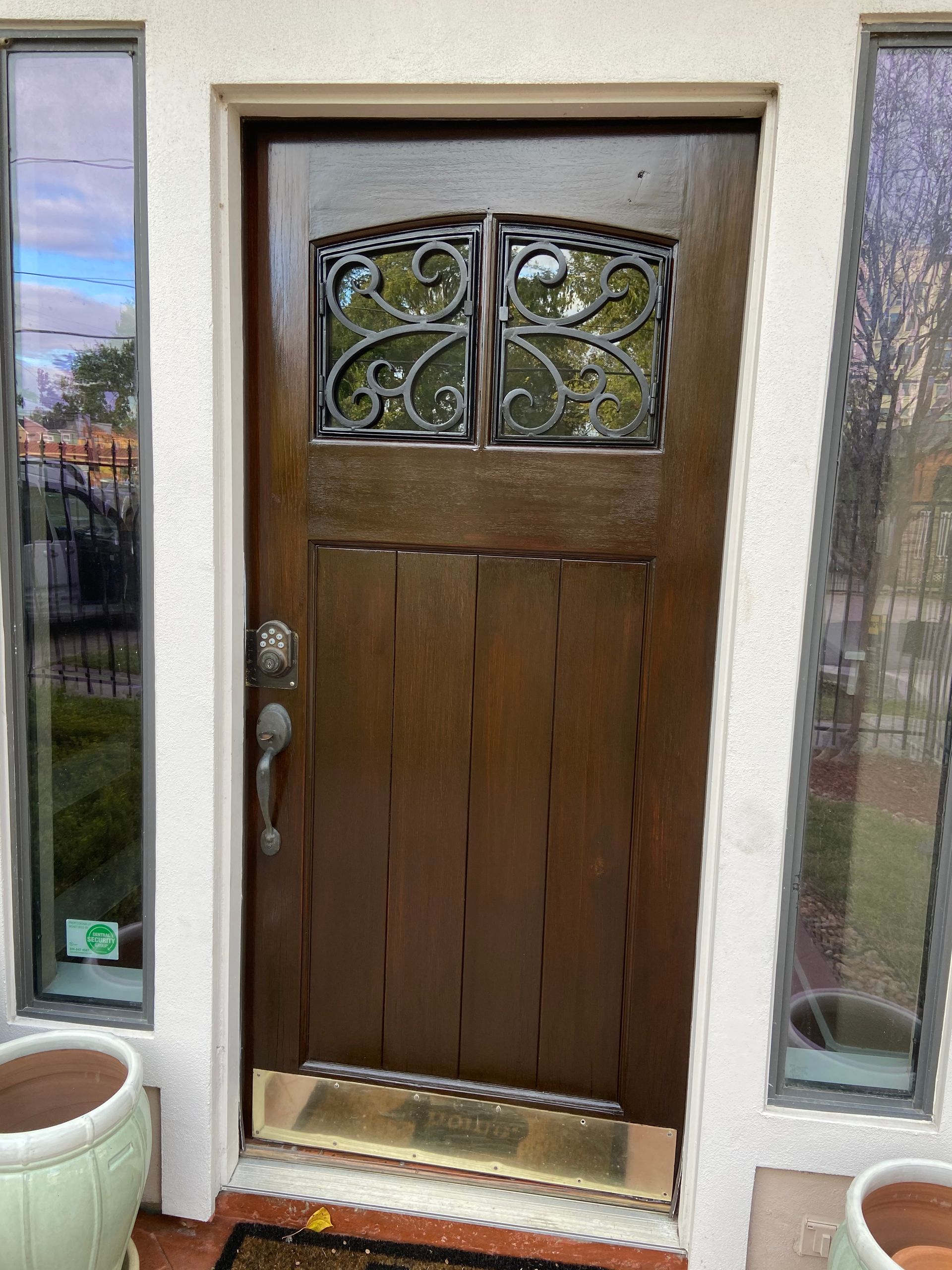 A brown door with a wrought iron design is sitting on a porch next to potted plants.