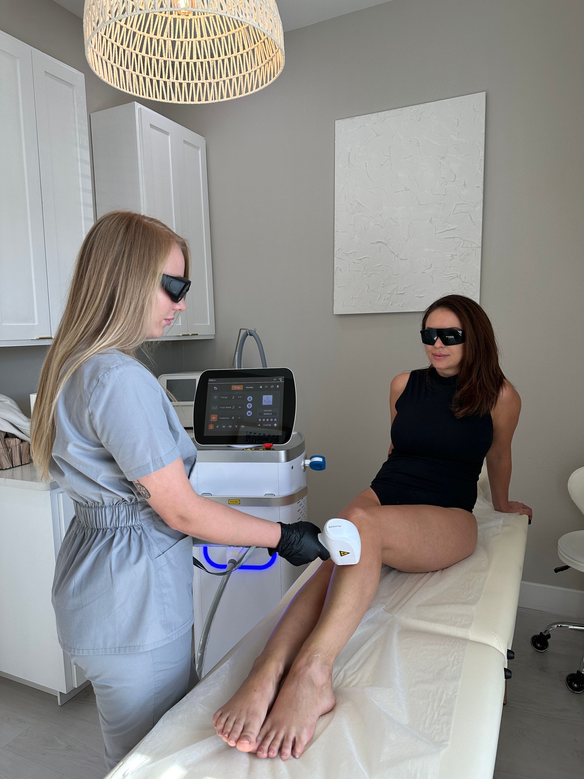 A woman is getting her legs waxed by a woman wearing sunglasses.